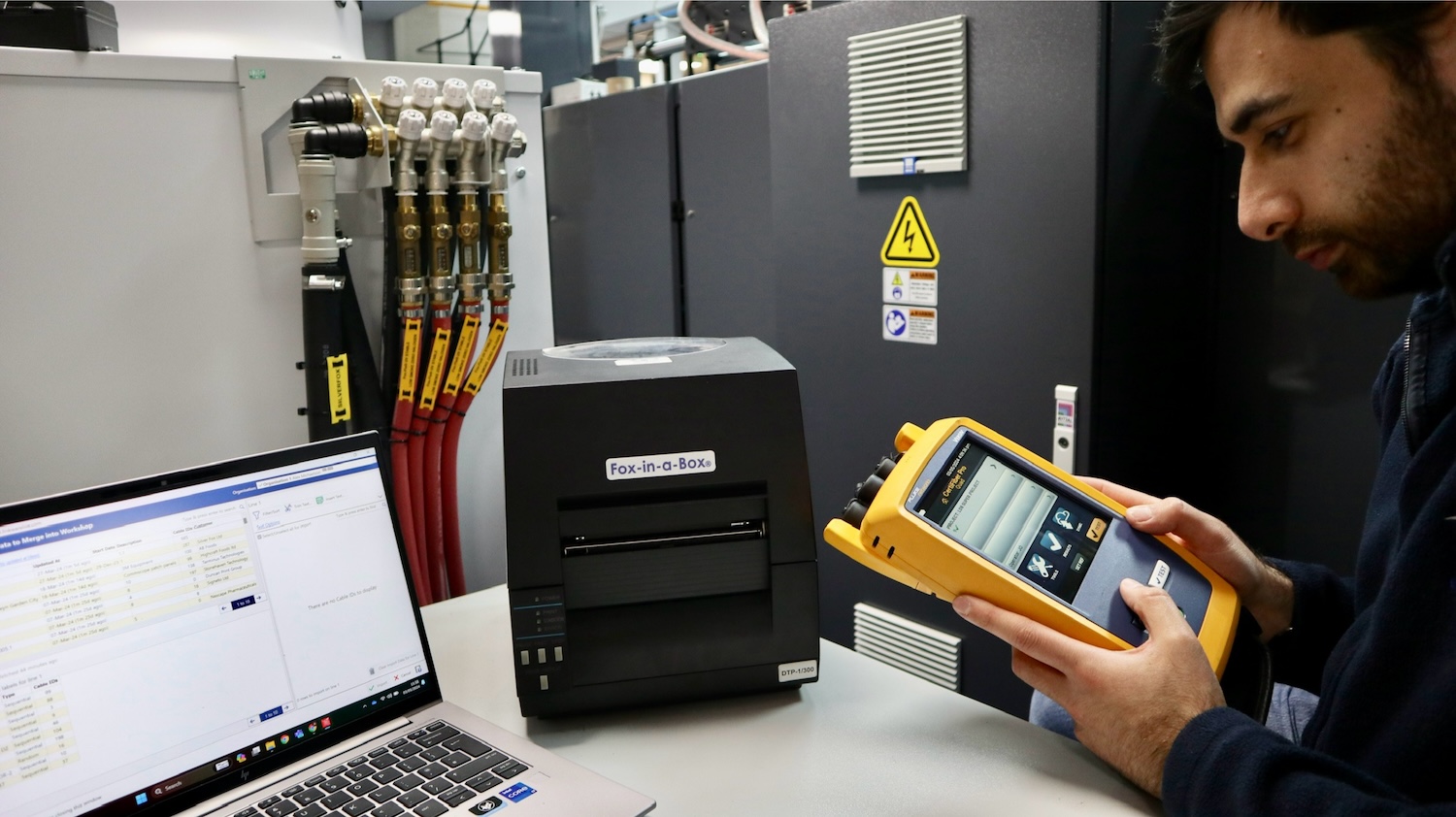 Man works with a Versiv tool in front of a desktop holding a laptop and a thermal printer